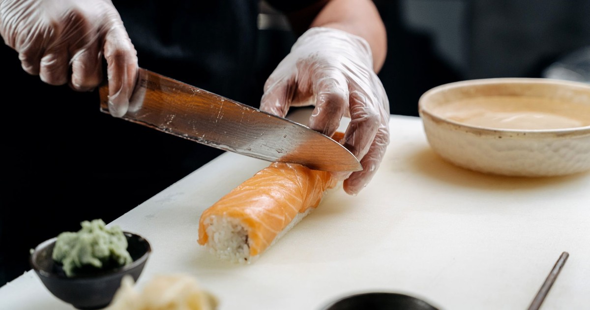 Close-up of a chef slicing a salmon sushi roll with precision, showing fresh ingredients.
