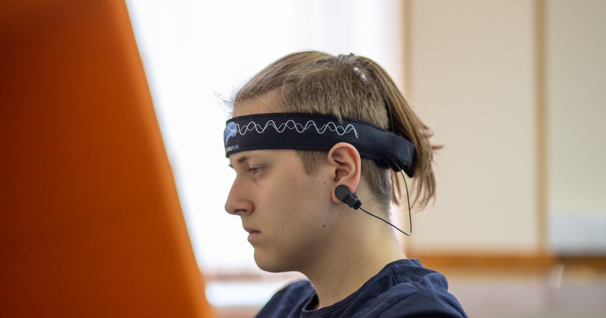 A young man using a headband EEG device while focused on his studies indoors.