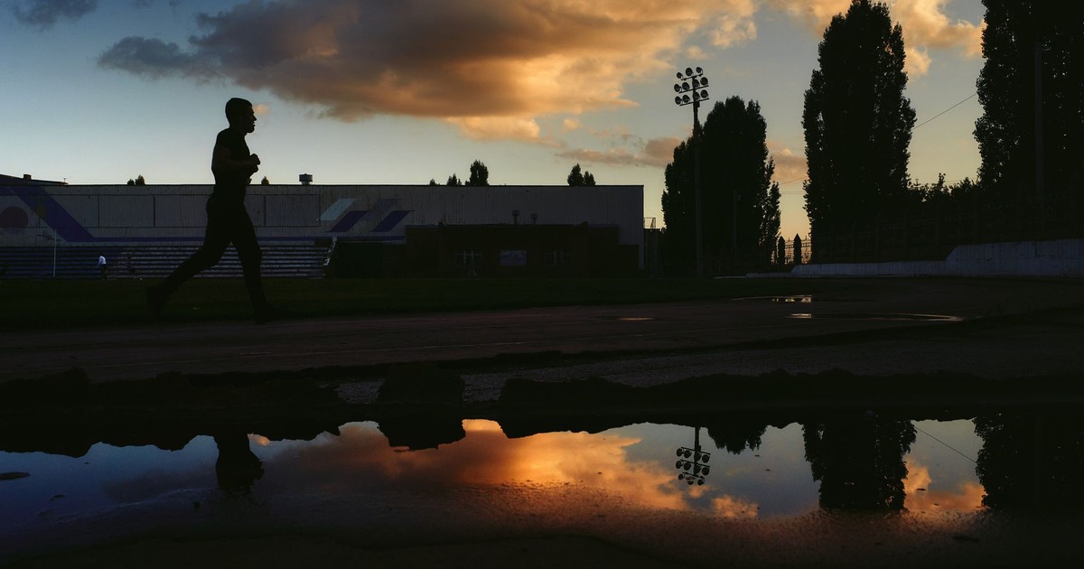 A silhouette of a man running on a track with a dramatic sunset sky reflected in puddles.