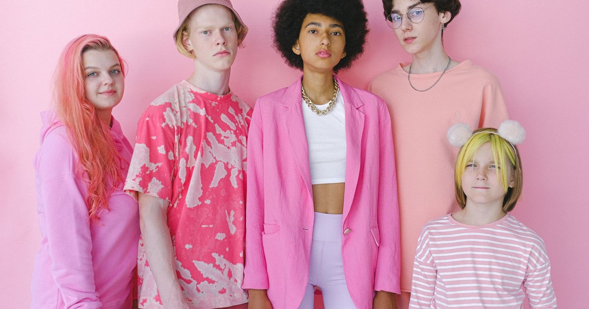 Group of multiracial teenage boys and girls looking at camera on pink background of studio