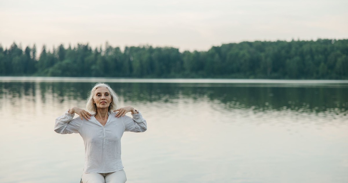 A senior woman practicing yoga by a serene lake, promoting healthy aging.