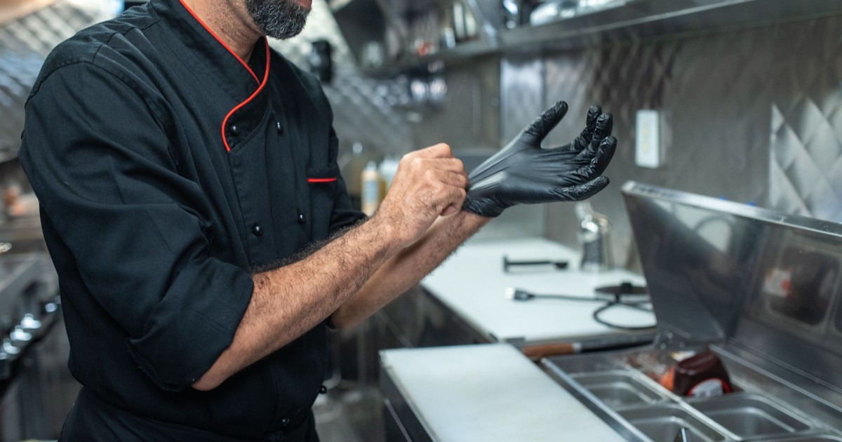 Chef putting on gloves in a professional kitchen setting, emphasizing hygiene and readiness.