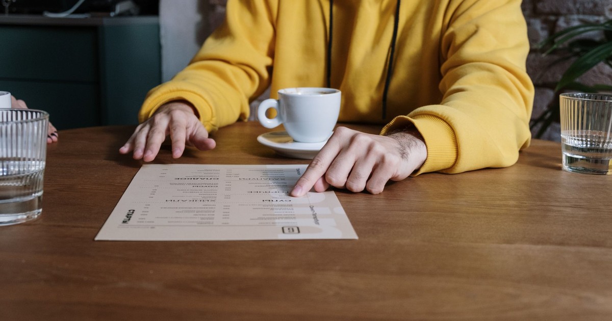 A person wearing a yellow hoodie points to a menu in a cozy cafe setting.