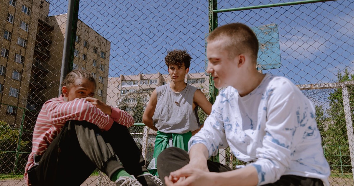 Three teenagers sitting and relaxing on an outdoor basketball court on a sunny day.