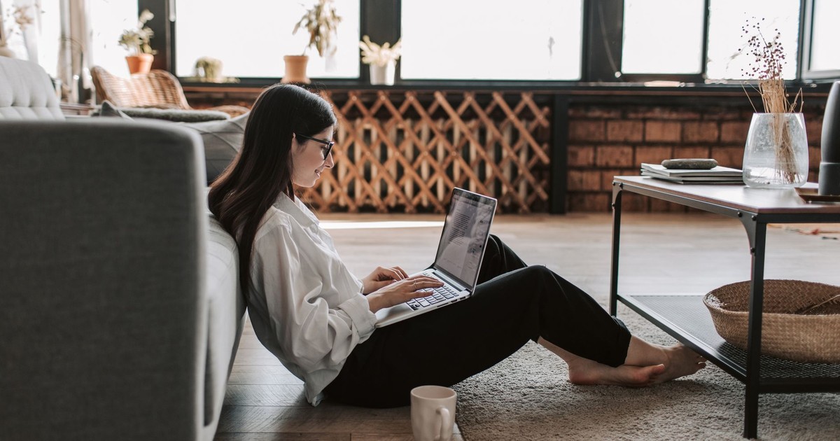 A young woman working from home using a laptop in a relaxed living room setting.