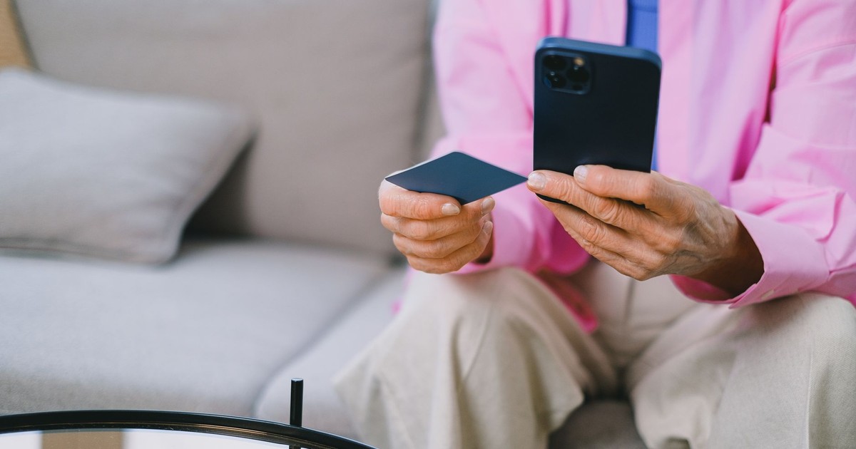 Elderly person making an online payment with credit card using smartphone, seated indoors.