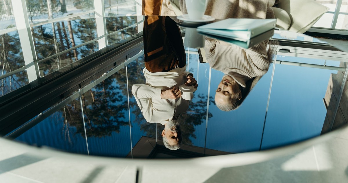 Reflection of an elderly couple enjoying coffee together in a modern sunlit interior.