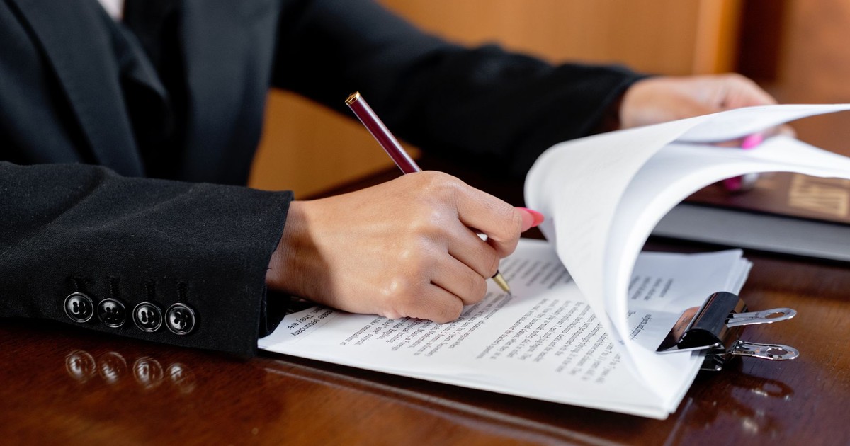 Close-up of a woman signing legal documents with a pen in an office setting.