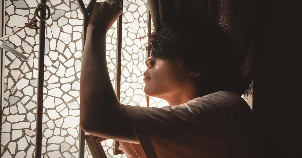 Side view of a young man posing thoughtfully by a mosaic glass window with soft light.
