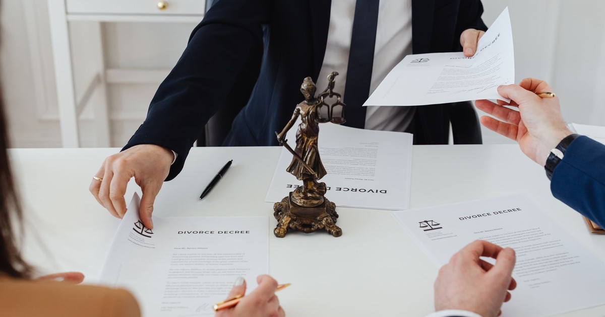 Three adults discussing divorce documents in a formal office setting with legal statue in view.