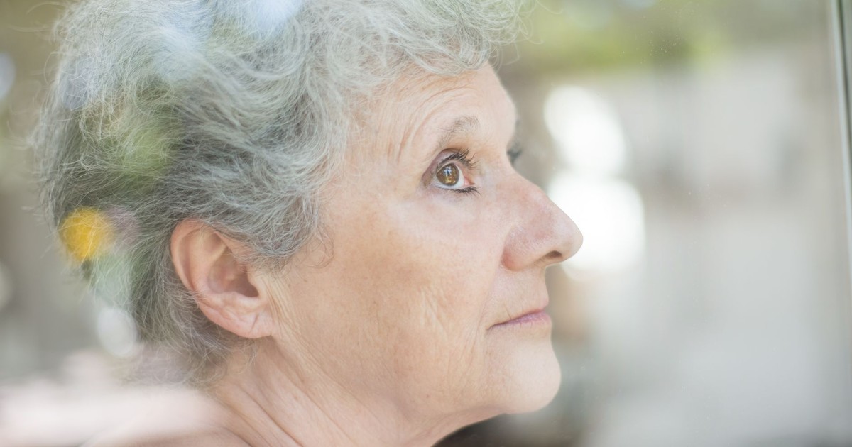 Close-up of an elderly woman with gray hair looking thoughtfully through a window.