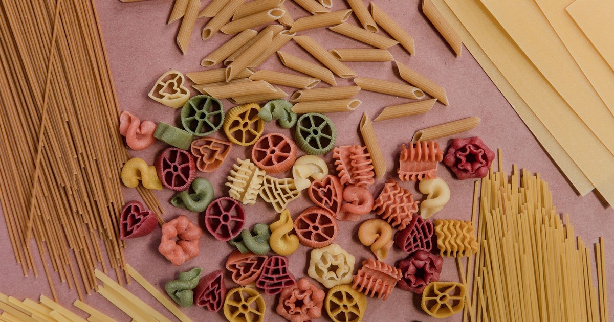 Close-up of assorted uncooked pasta in various shapes and colors on a surface.