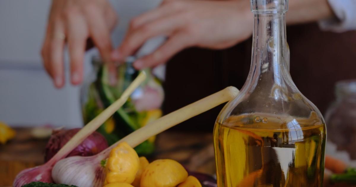 Hands preparing vegetables with olive oil, garlic, and squash in a kitchen setting.
