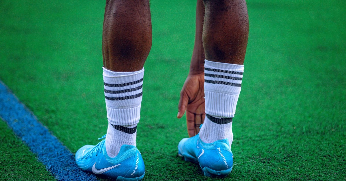 Athlete stretching on green field in blue cleats and striped socks, preparing for game.
