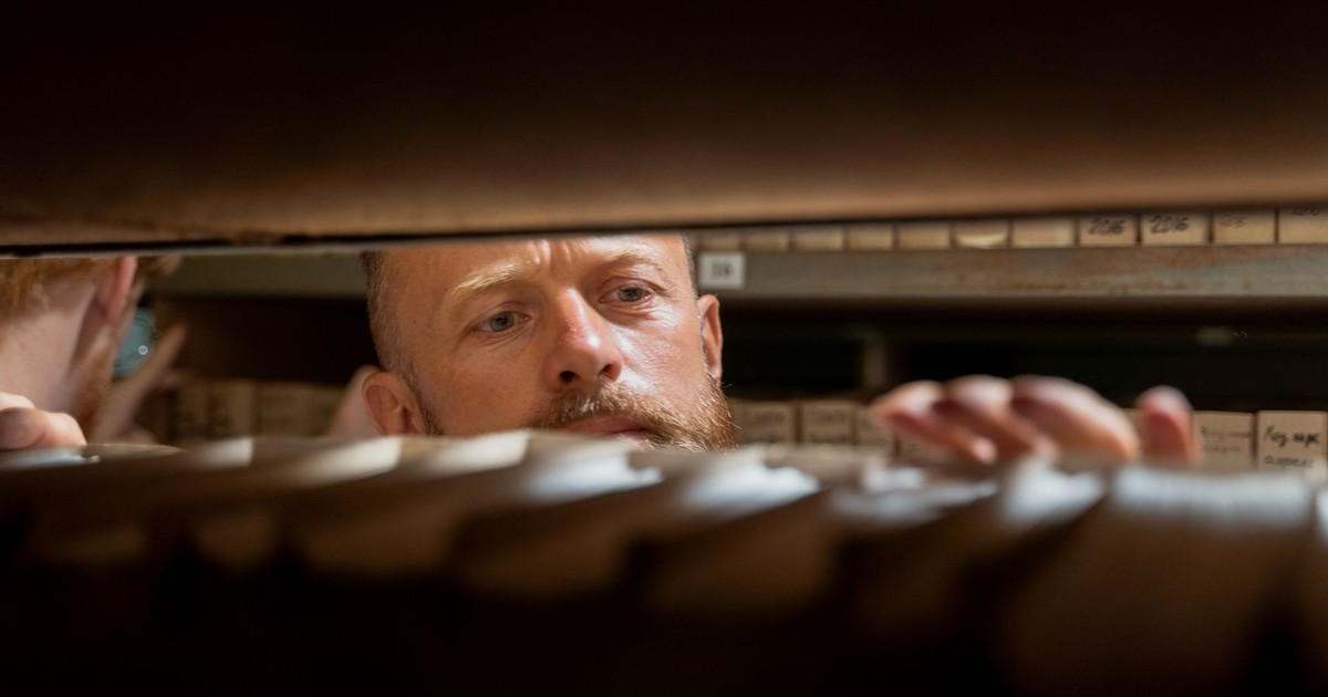 A man searches through archives in an office storage room, focused and working.