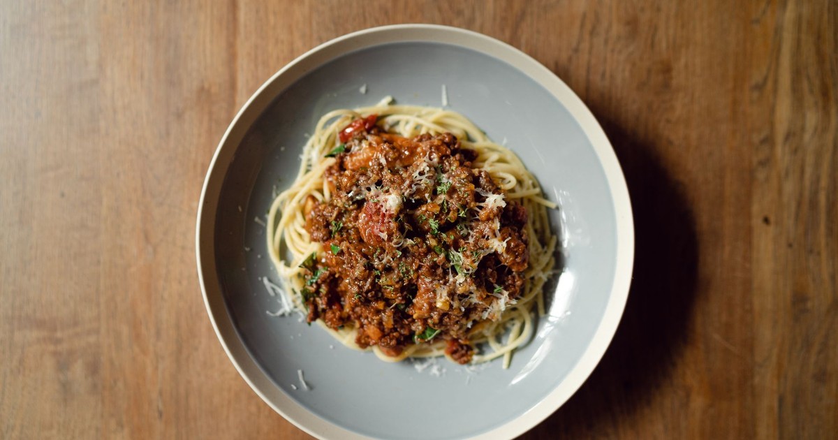 Top view of round plate with delicious Italian pasta Bolognaise garnished with grated parmesan cheese placed on wooden table
