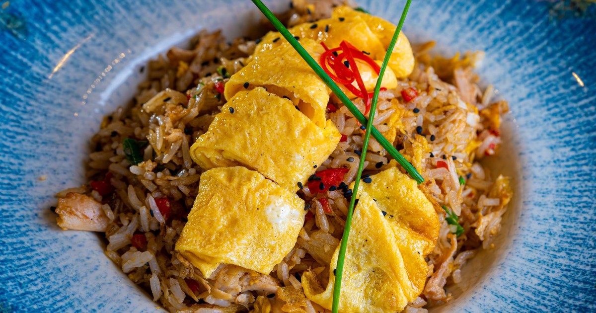 Fried rice topped with a neatly sliced omelette and garnished with chives and chili.