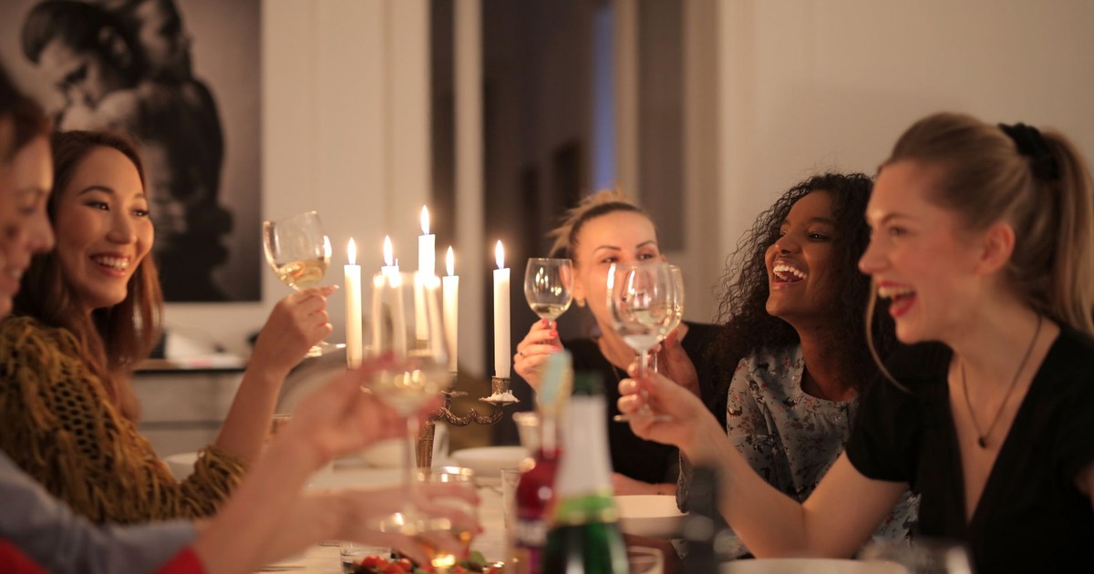 A group of women enjoying a lively dinner party with wine and candlelight, showcasing friendship and happiness.