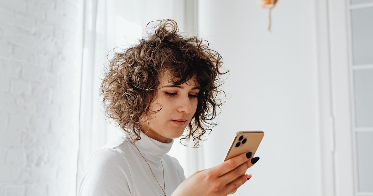 A young woman with curly hair using a smartphone indoors. Natural light and modern decor.