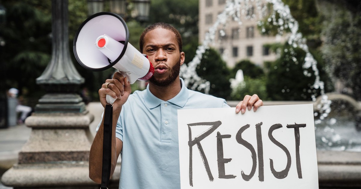 A man stands at a protest with a megaphone and a sign that reads 'RESIST', advocating for social change.