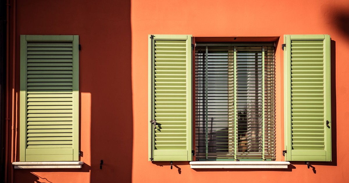 A modern exterior with green shutters against a vivid orange wall, showcasing contemporary design.