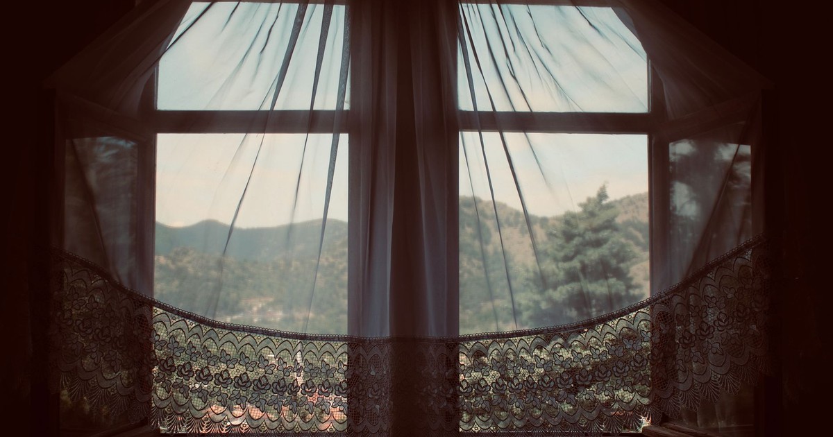 Serene landscape through a vintage window with lace curtains, capturing the peaceful outdoors.