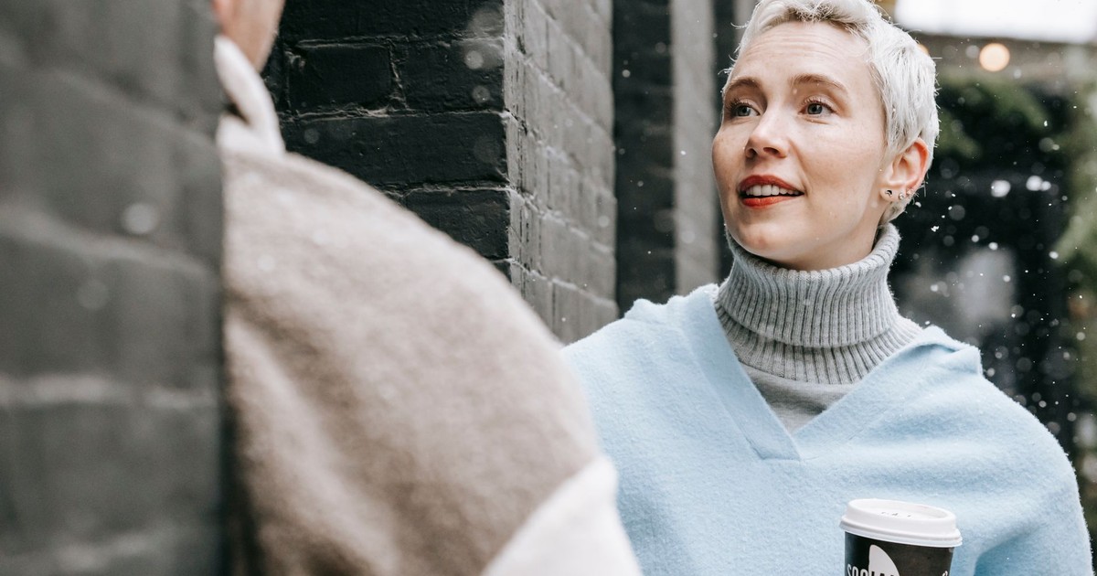 Adult female with hot drink to go speaking with crop unrecognizable male partner on city street in daylight