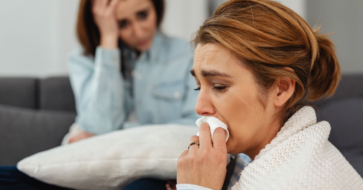 Two women sitting on a couch, expressing and sharing emotions of sadness and support.