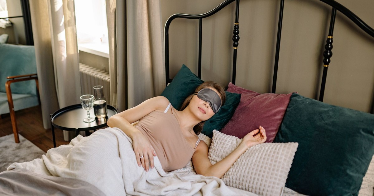 Woman sleeping comfortably in bed with an eye mask and pillows.