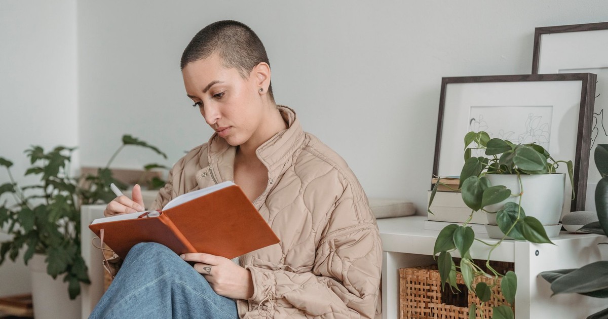 Young female with tattooed ring and short hair taking notes in agenda while sitting in house room
