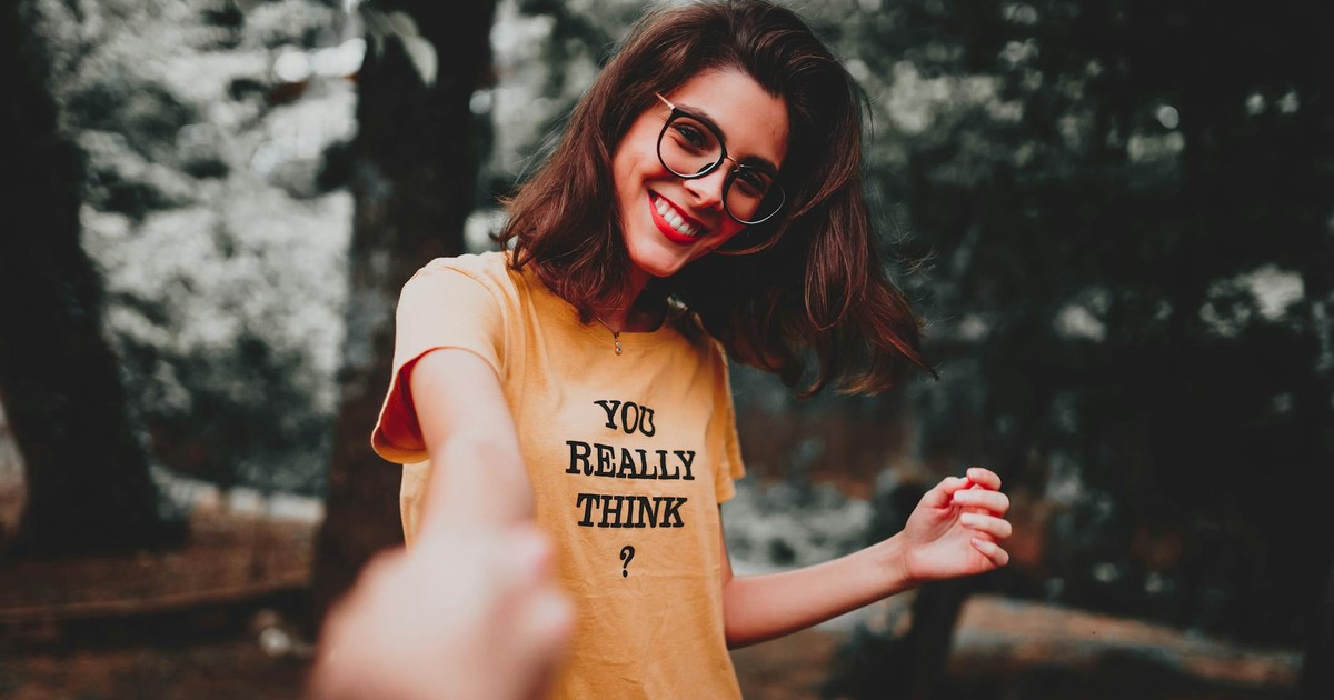 Cheerful woman in glasses holding hands outdoors, wearing a text t-shirt.