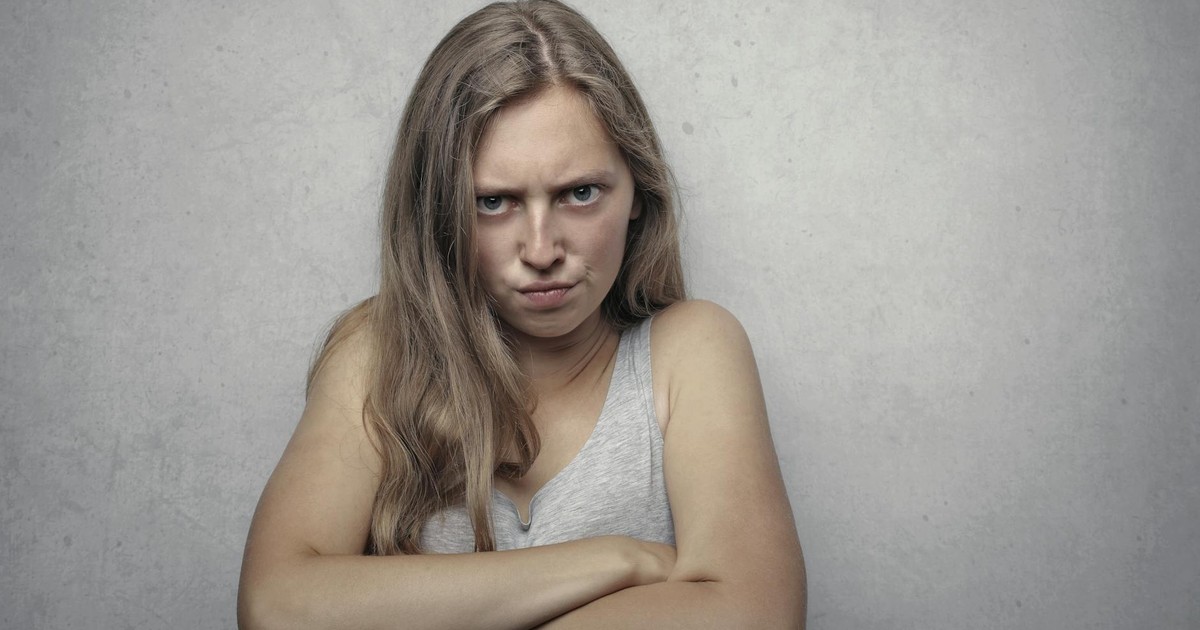 A woman with arms crossed showing a fierce expression against a gray background.