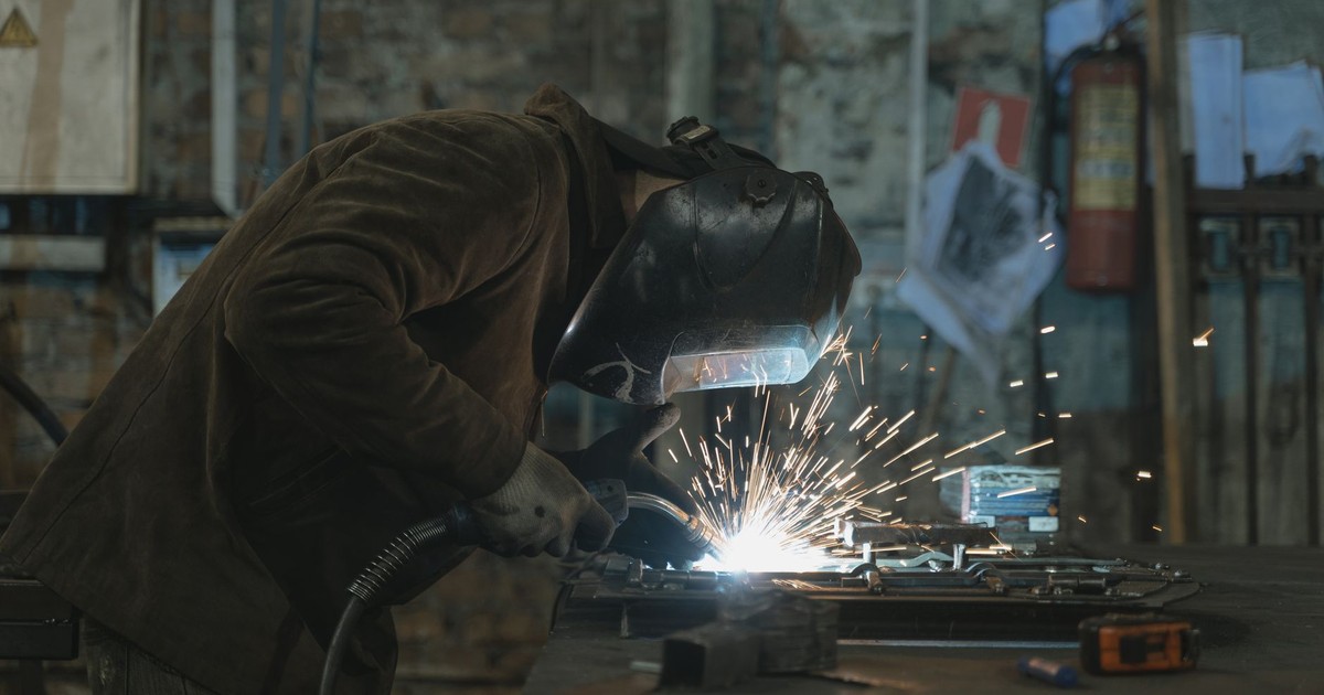 A skilled welder focused on welding a metal piece in an industrial workshop. Sparks flying vividly.