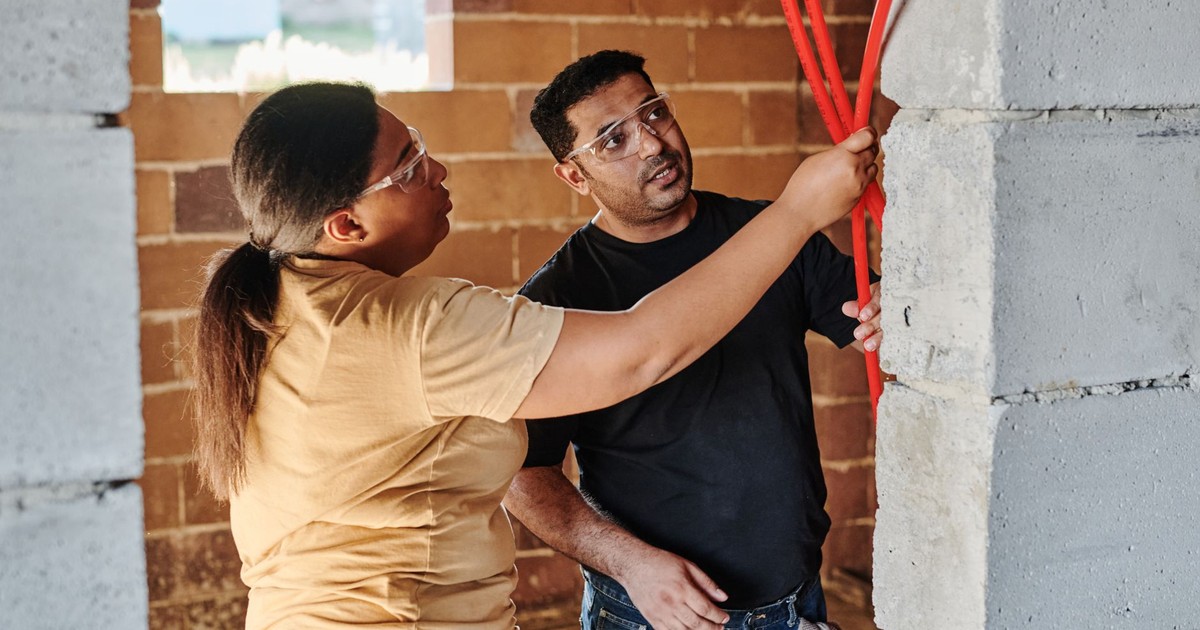 Two construction workers assessing electrical wiring in a brick structure.