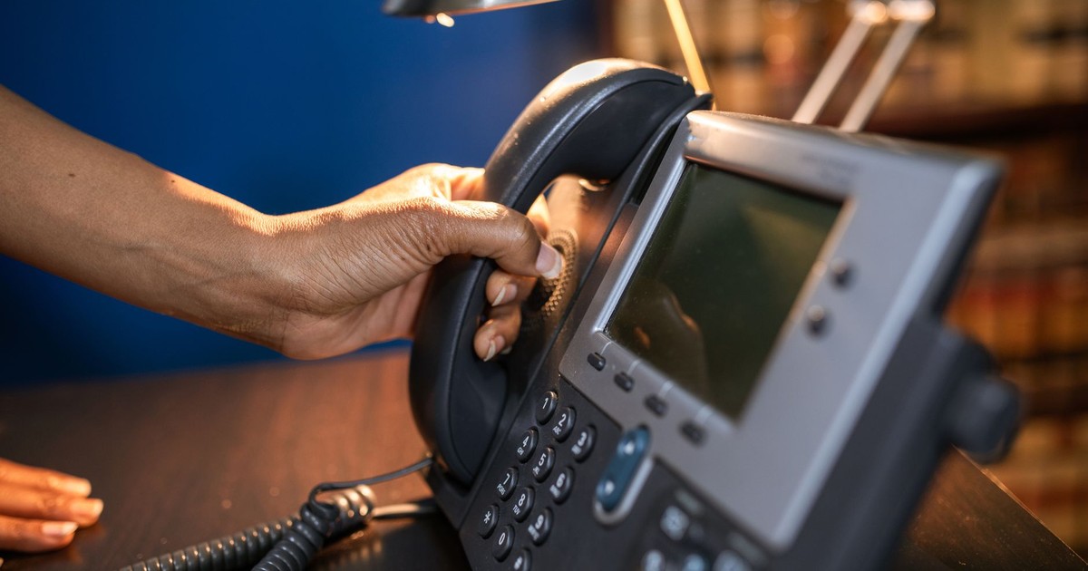 A close-up image of a hand picking up a handset from an office telephone, emphasizing communication device usage.