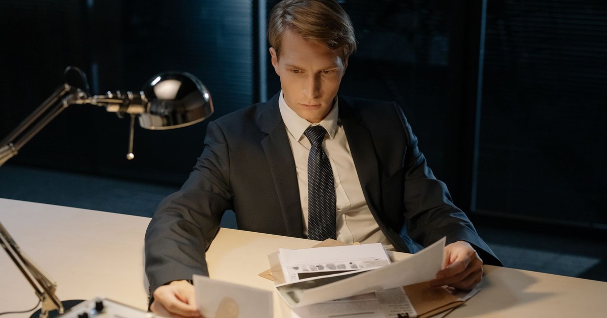 Focused investigator reviewing evidence in a dimly lit office setting.