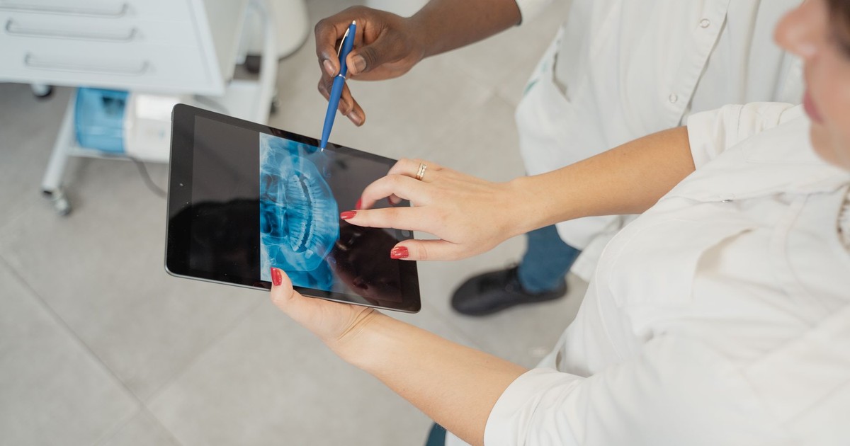 Dentist examining a dental x-ray on a tablet with patient in a modern clinic.