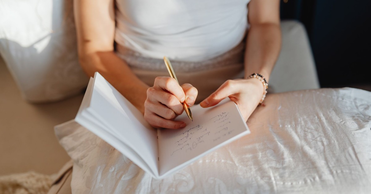 Close-up of a woman writing in a journal while sitting comfortably indoors.