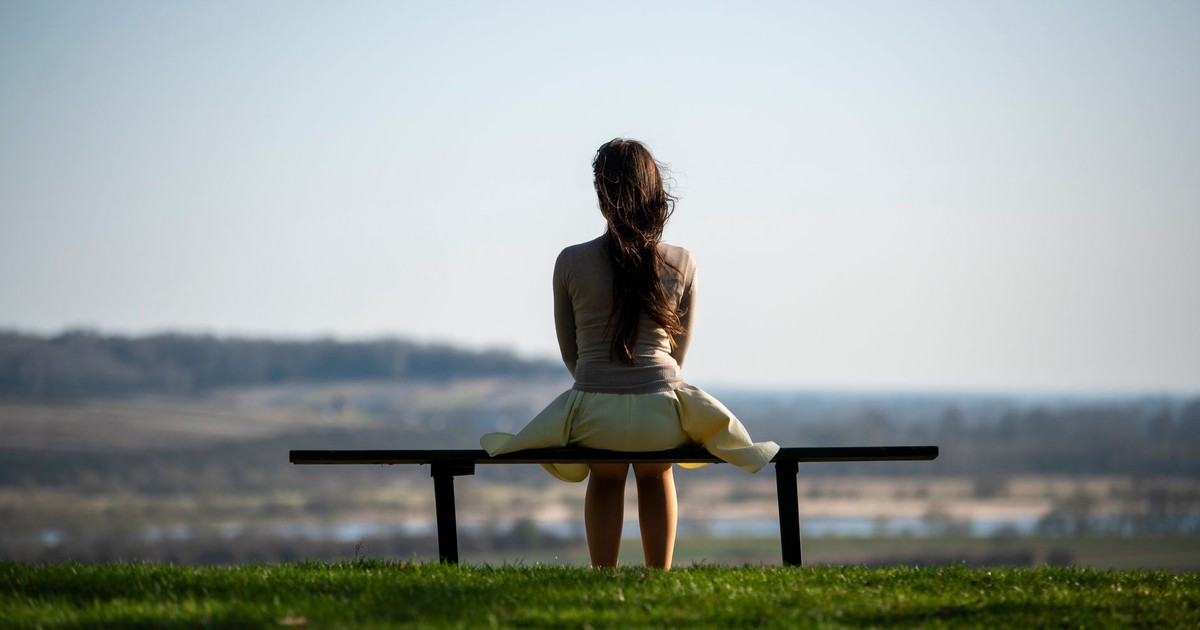 Serene image of a woman sitting on a bench overlooking a scenic field, symbolizing solitude and reflection.