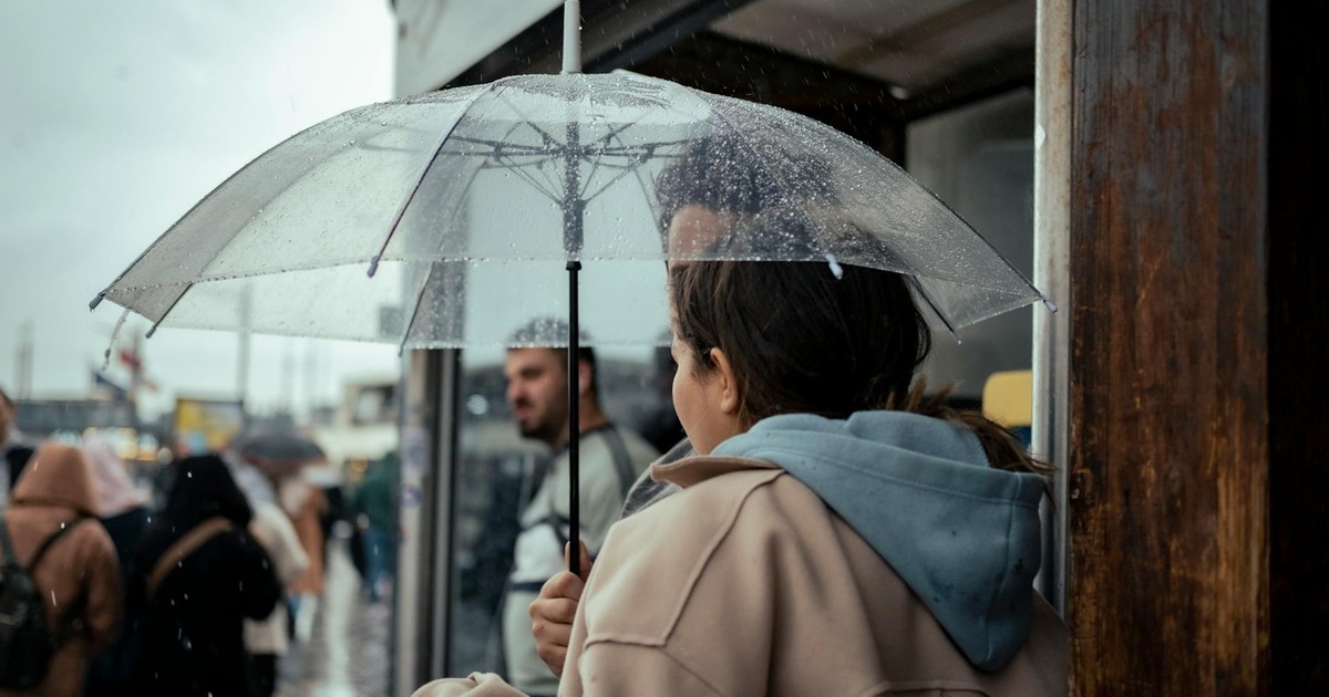 A bustling urban street with people using umbrellas under rainy weather at a bus stop.