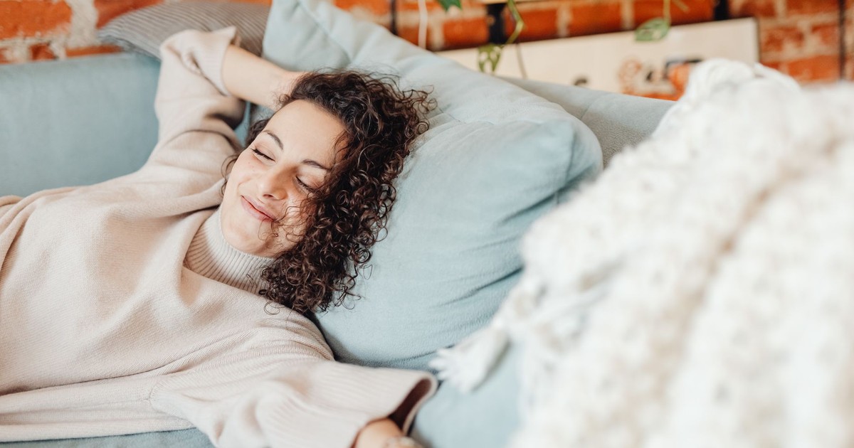 Woman with curly hair relaxing on a comfortable sofa in a cozy indoor setting.