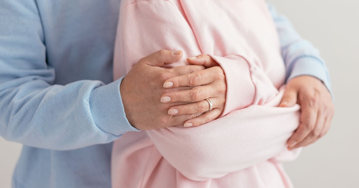 A tender embrace captured in a close-up, displaying affection with hands wrapped in pastel sweaters.