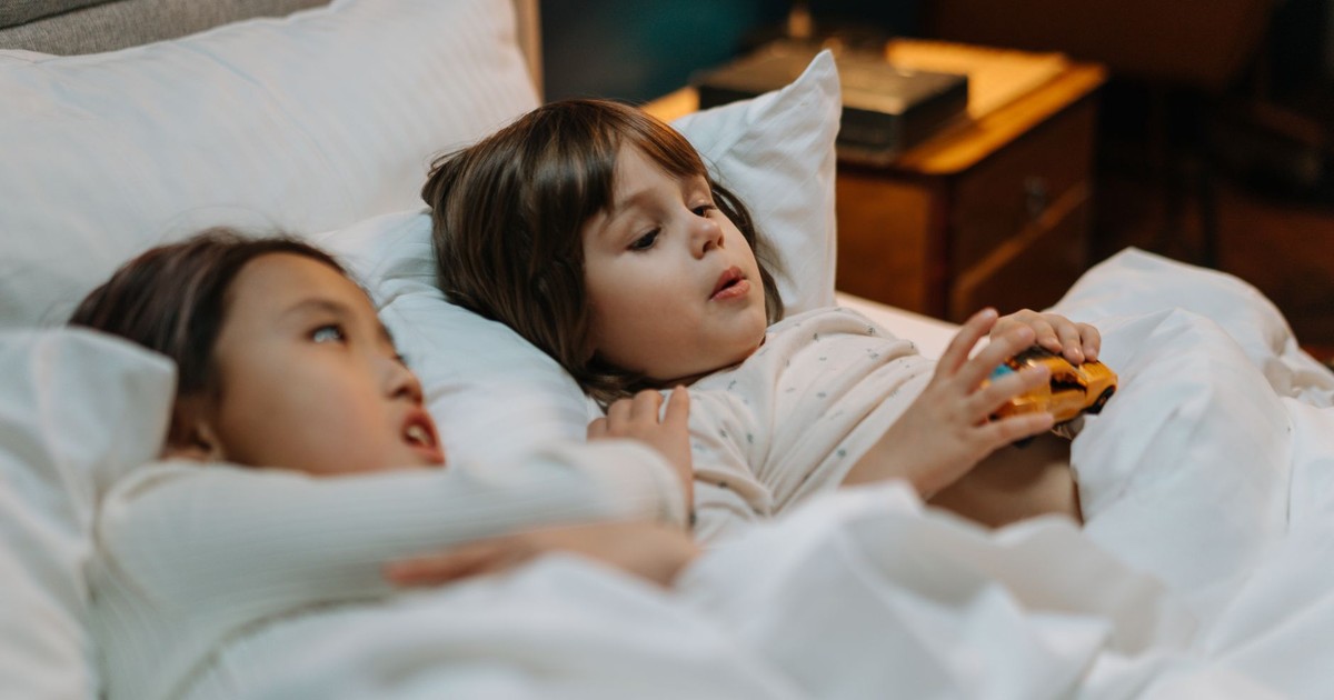 Two kids in bed playing with a toy car, enjoying a cozy moment indoors.