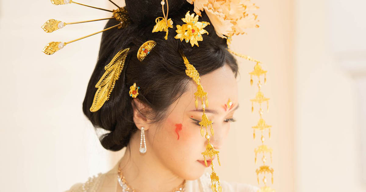 A woman adorned with ornate Asian headpieces and elegant jewelry in a classic pose