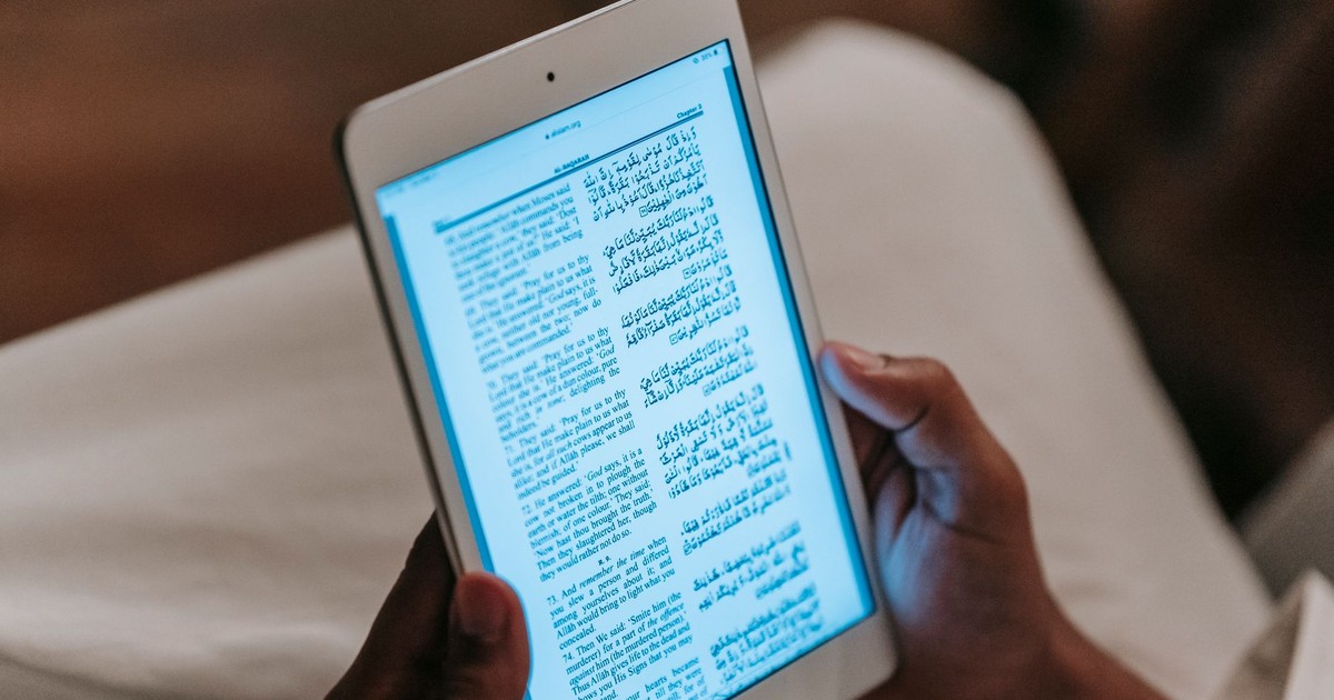Crop unrecognizable person in casual clothes reading text on tablet against blurred background in room
