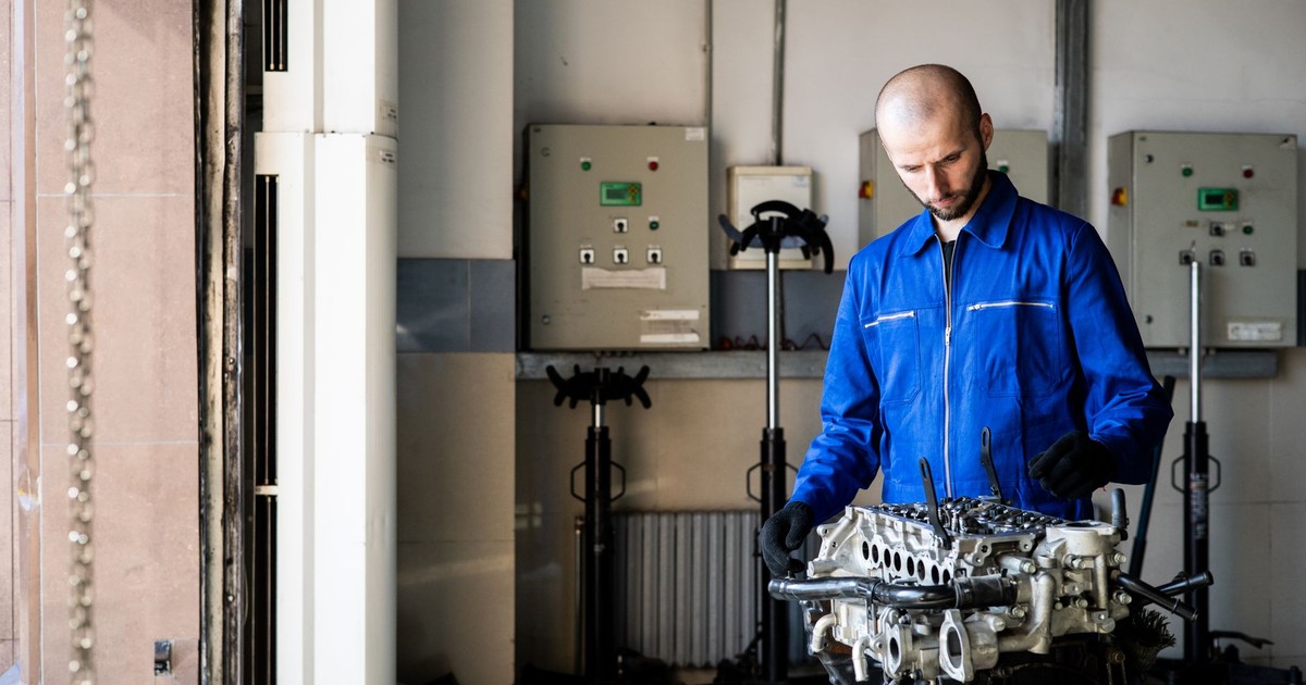 A mechanic in blue coveralls inspects an engine in a repair shop.