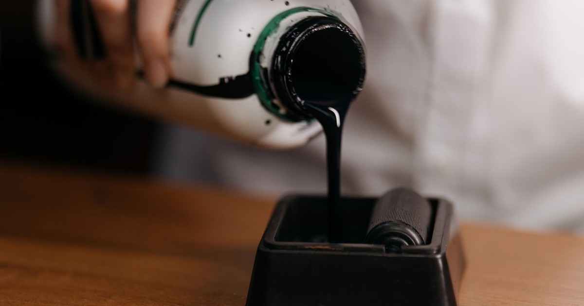 A close-up image of ink from a bottle being poured onto a roller, highlighting art supplies.