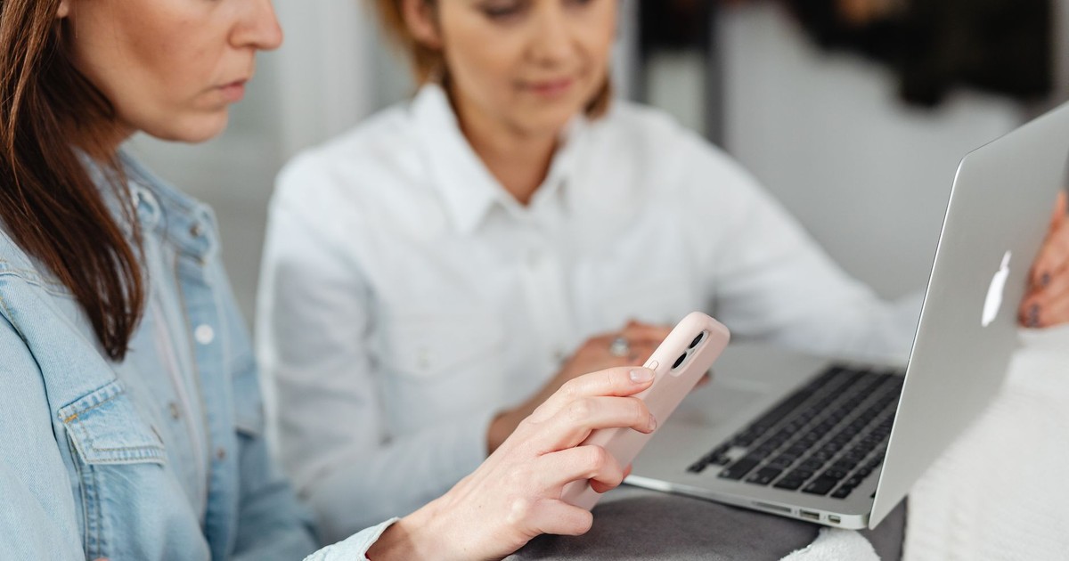 Two women working together using a laptop and smartphone in a casual setting.