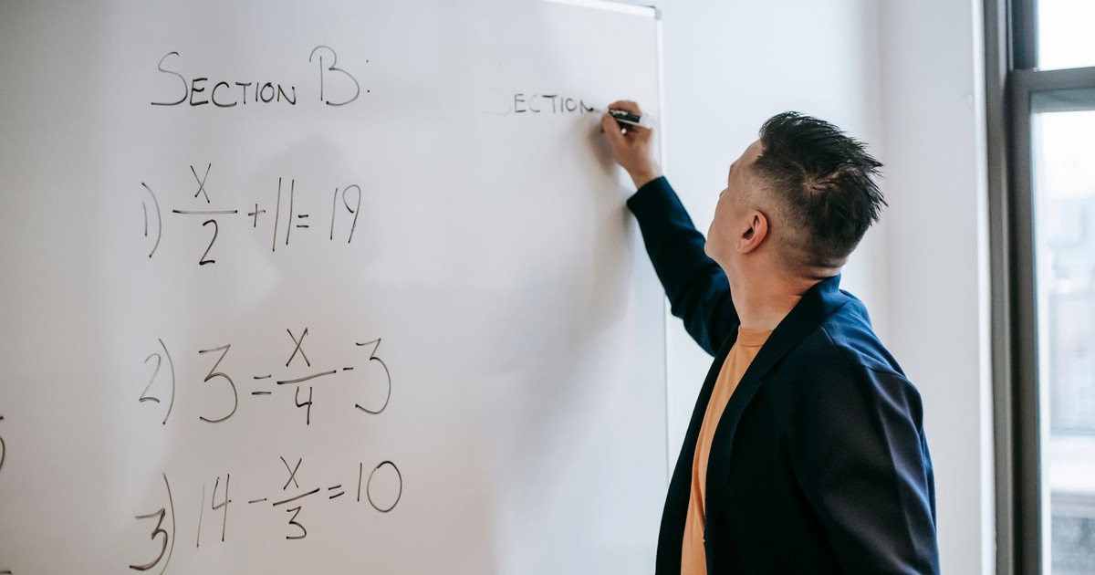Side view of focused teacher in jacket writing equations on whiteboard in light room in daylight