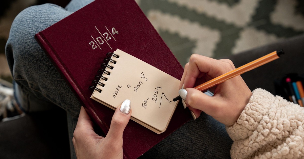 Woman writing future plans in a 2024 planner with focus on personal goals and organization.